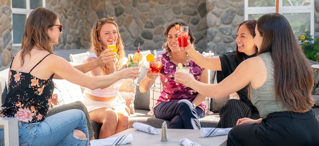 Team members sits outside on a sunny patio in Canmore, cheersing their cocktails on day one of their corporate retreat.