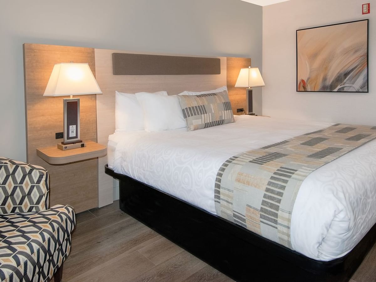 Hotel room with king bed, lamps, arm chair, and art on the wall