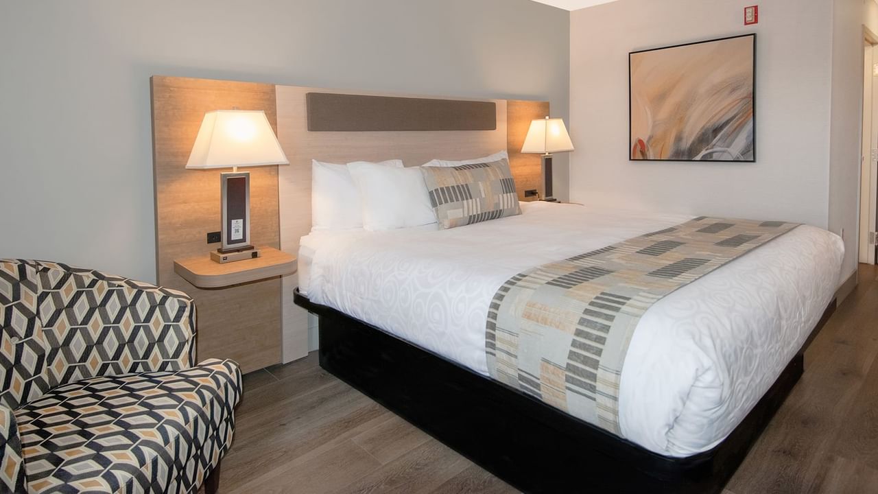 Hotel room with king bed, lamps, arm chair, and art on the wall