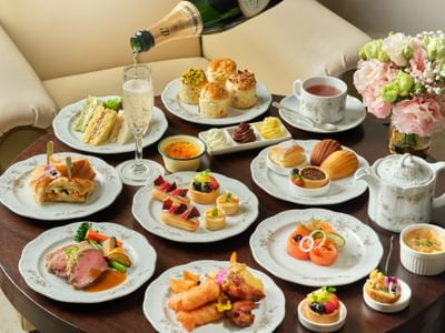 Champagne pouring into a flute glass by assorted sweet pastries and savory platters on a table at Goodwood Park Hotel