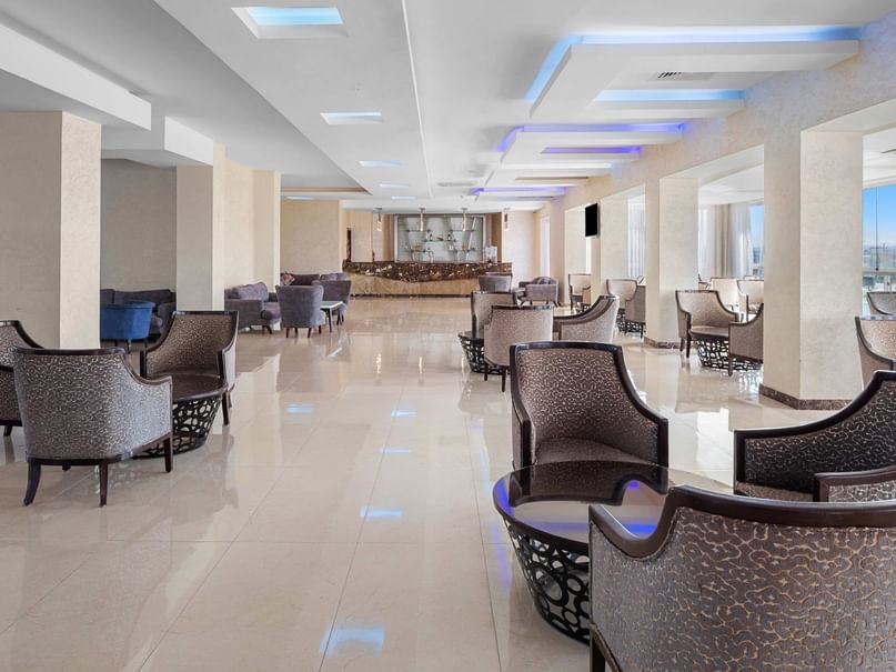 Lounge area with many chairs, a tiled floor, and a glass wall showing the outdoors.