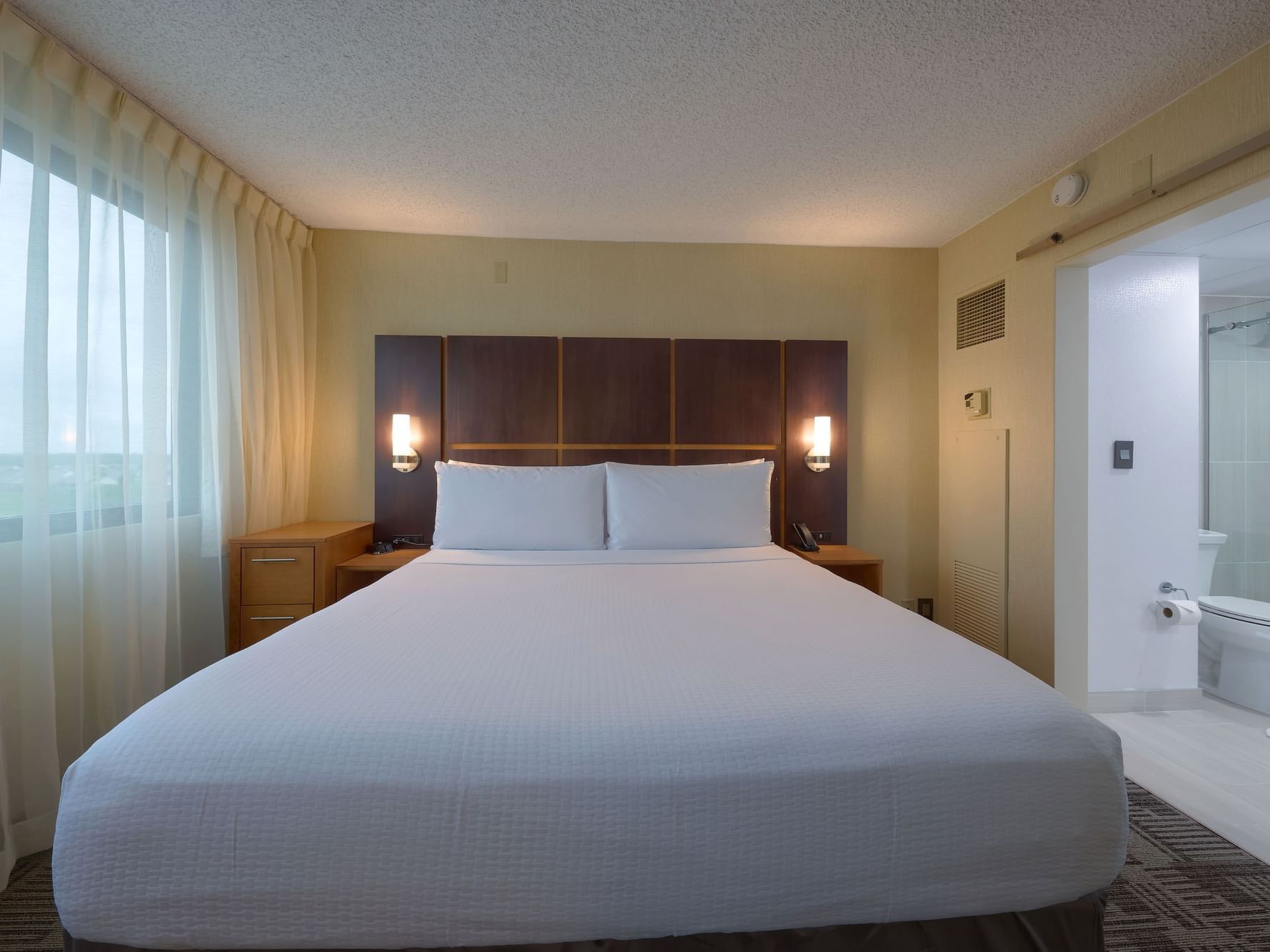 Premium King Room with a large bed, nightstands, and a bathroom at the NCED Conference Center in Norman, OK.