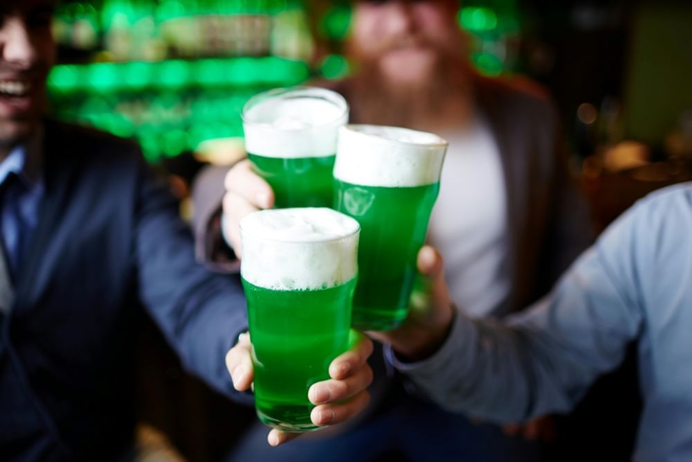 Three out-of-focus men hold three pints of green, frothy beer together.  