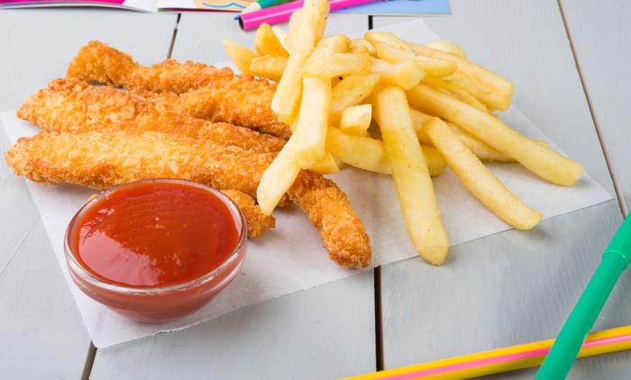 Crispy chicken strips in a basket by fries on white paper featuring Camo Eats at Anaheim Portofino Inn & Suites