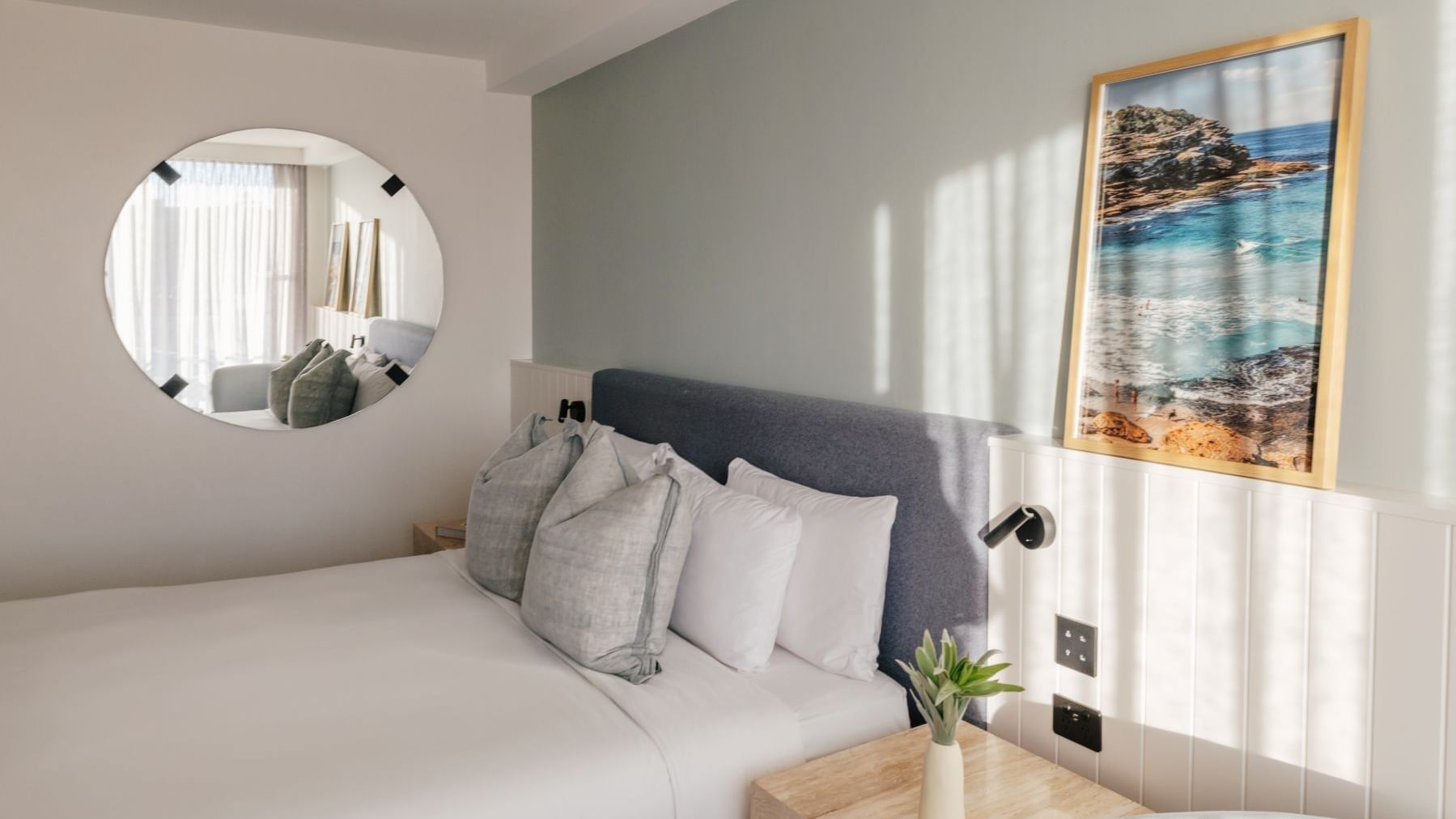 Sunset View King – Elysium Floor at Elysium Hotels with pillows by a round mirror under a framed coastal photo on the wall
