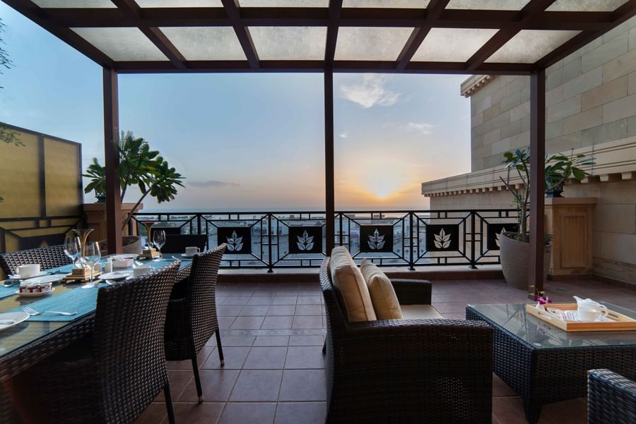 Dining area on a terrace by wicker sofas under a pergola at sunset in Penthouse Villa at Warwick Al Khobar