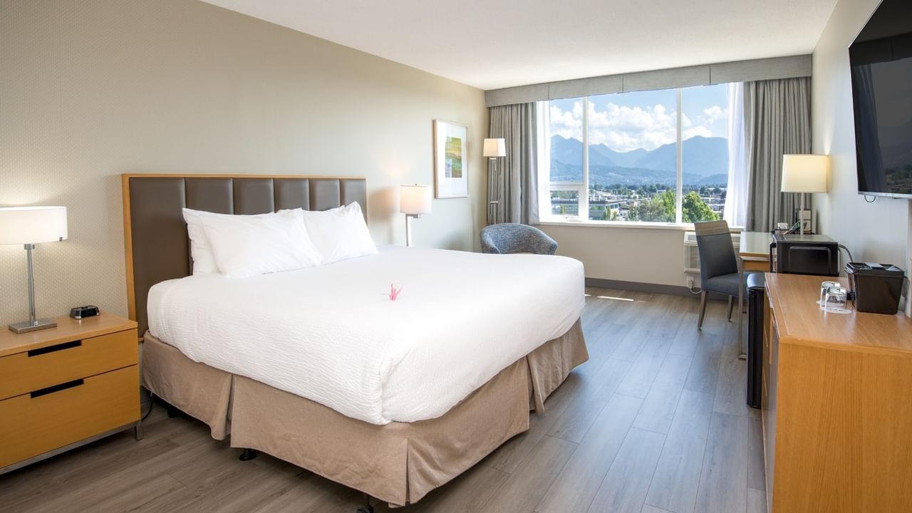A hotel room with a king bed, large window, and pond view.