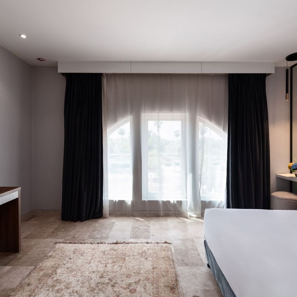 Junior Suite City View features a bed under black curtains, near a console with a TV at Warwick Al Jubail