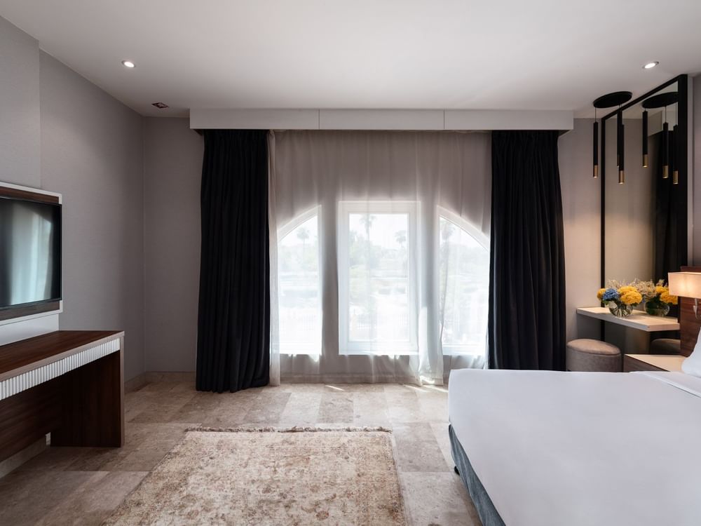 Junior Suite City View features a bed under black curtains, near a console with a TV at Warwick Al Jubail