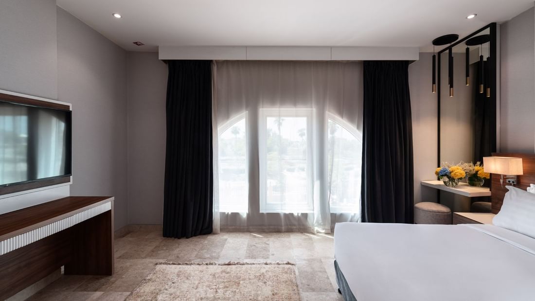 Junior Suite City View features a bed under black curtains, near a console with a TV at Warwick Al Jubail