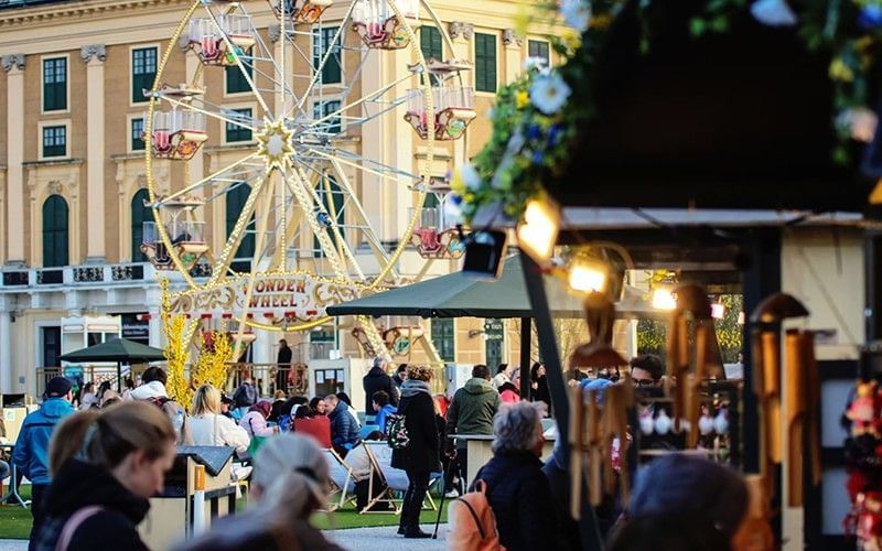Belebter Ostermarkt vor Schloss Schönbrunn mit Marktständen, Besuchern und Riesenrad.