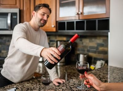 Man pouring red wine from a bottle into a glass in a modern kitchen at Blackstone Mountain Lodge