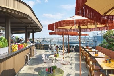 Rooftop terrace dining area with colorful parasols, cozy tables, and a vibrant bar in Chez Bernard at Hotel Motto Vienna