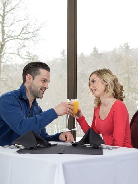 Couple toasting their drinks on a dinner table with an outdoor view at Cove Pocono Resorts