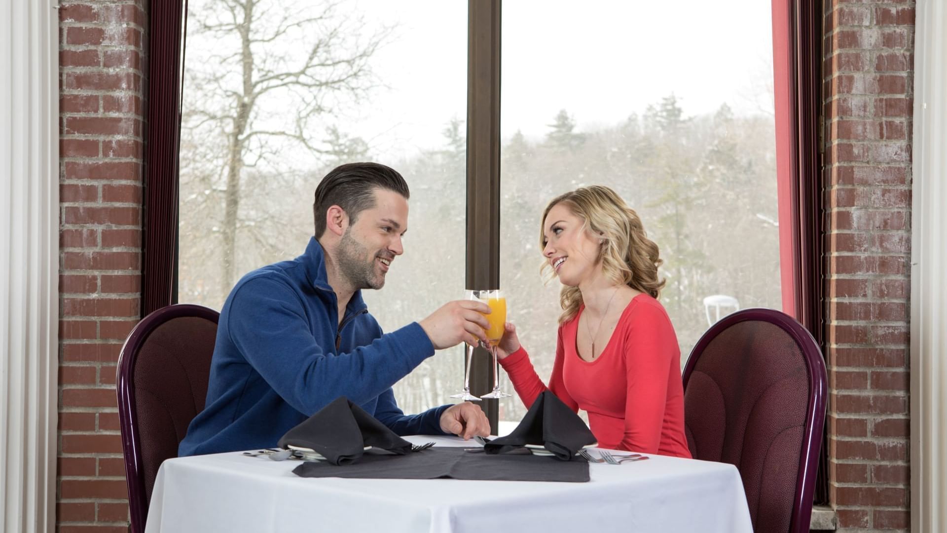 Couple toasting their drinks on a dinner table with an outdoor view at Cove Pocono Resorts