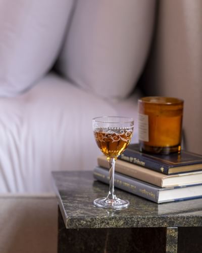 Glass of wine on a marble table with stacked books and a candle by a bed at The Ashbrook Hotel