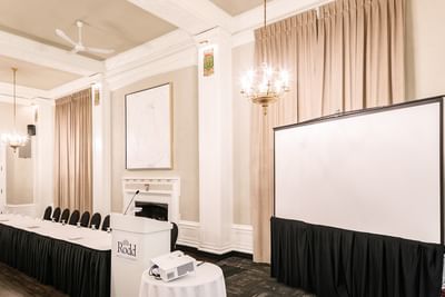 White podium by a projector screen under a classic brass chandelier in a meeting room at Rodd Charlottetown Hotel