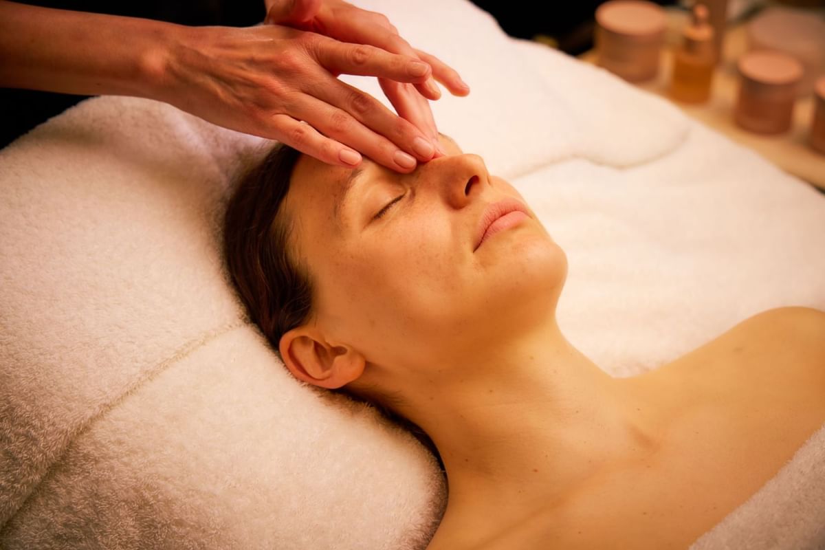 A woman lies on a spa table while a therapist applies a creamy facial mask at The May Fair Spa, The May Fair Hotel