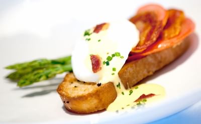 Poached egg with hollandaise sauce on toasted bread beside bacon slice and green asparagus spears at The Simsbury Inn