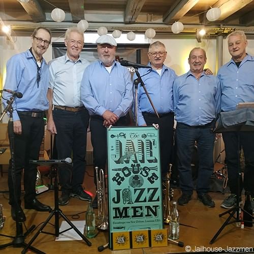 Musicians in blue shirts standing by a jazz band sign under lights on a stage at the Falkensteiner Hotel Montafon