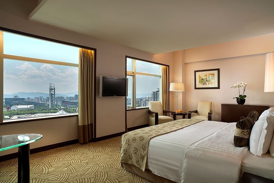 Guest room featuring city views through large windows and a white striped bed at Celebrity International Grand Hotel