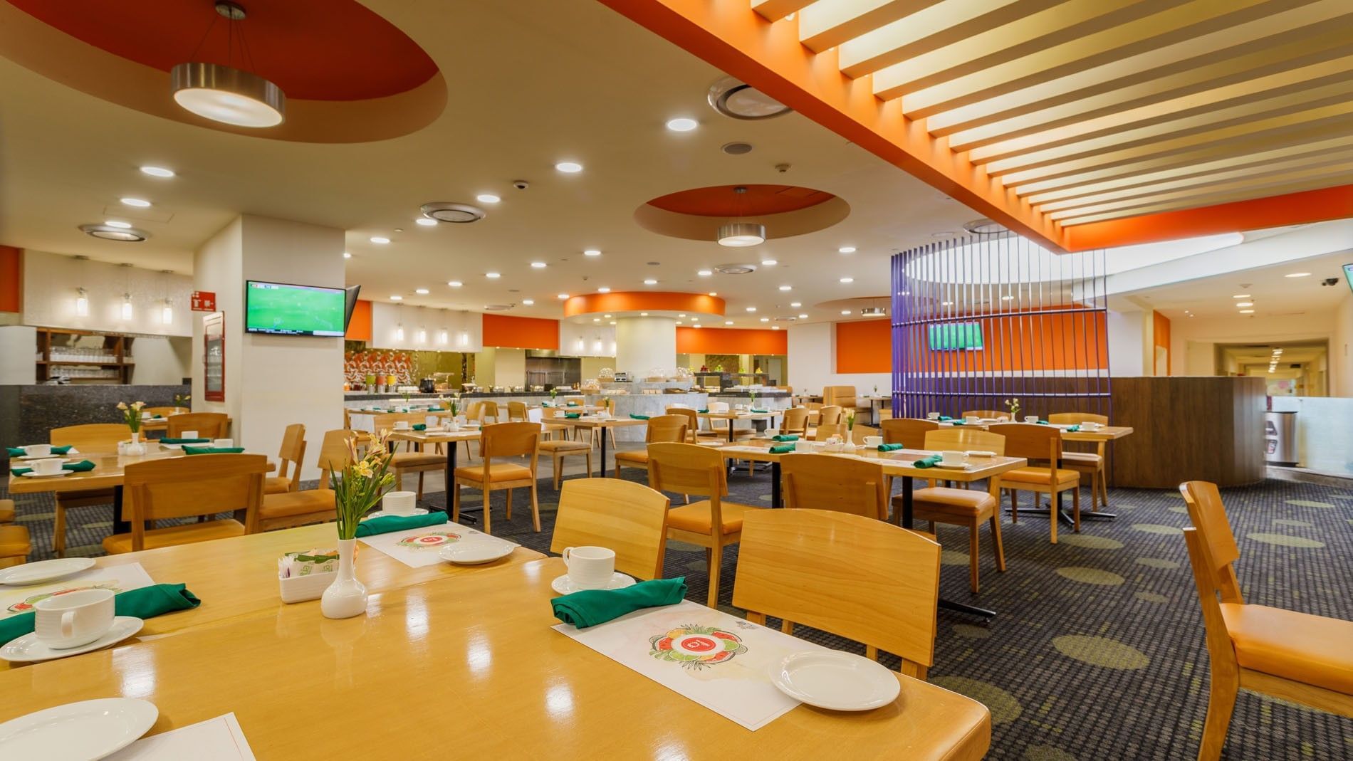 La Huerta breakfast area with wooden tables and orange accent wall decor at Camino Real Aeropuerto Mexico