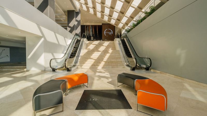 Grand lobby with orange benches by escalators, beneath a glass roof at Real Inn Tijuana