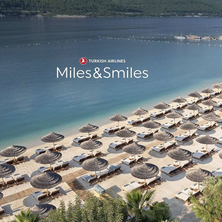 Aerial view of Titanic Luxury Collection Bodrum's beach resort with many sun loungers and umbrellas during the Spring Miles Campaign.