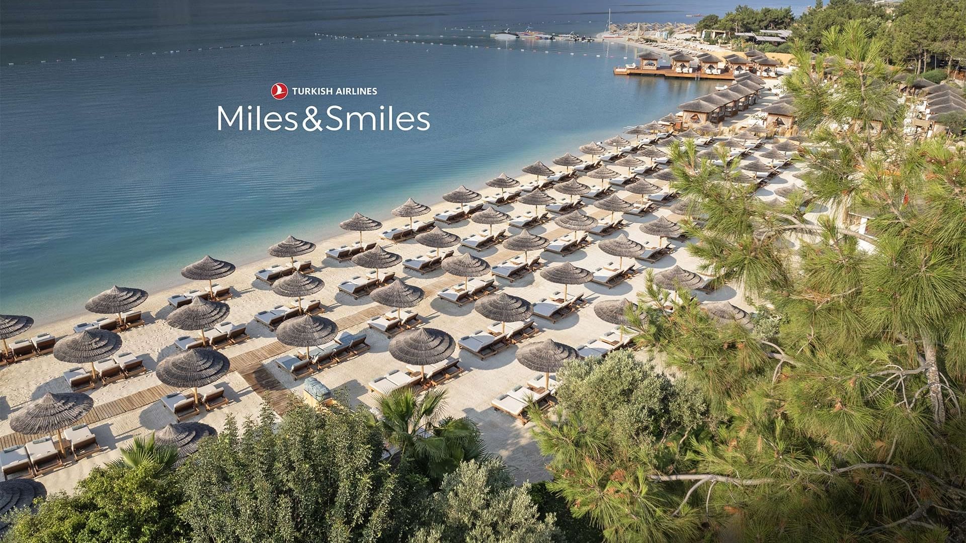  Aerial view of Titanic Luxury Collection Bodrum's beach resort with many sun loungers and umbrellas during the Spring Miles Campaign.