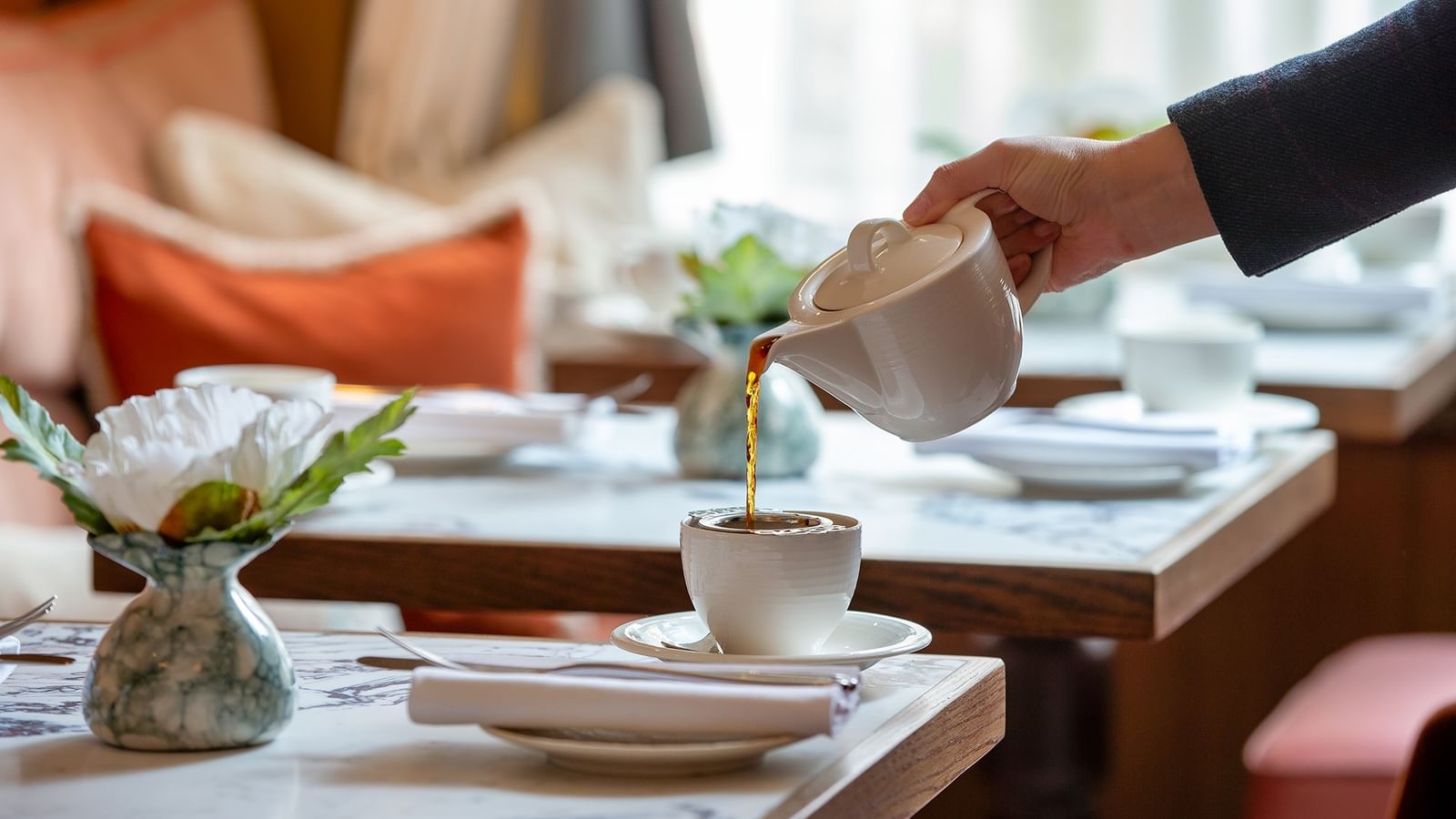 Hand pouring tea into a cup on a table set for afternoon tea at The Capital Hotel, Apartments & Townhouse London.