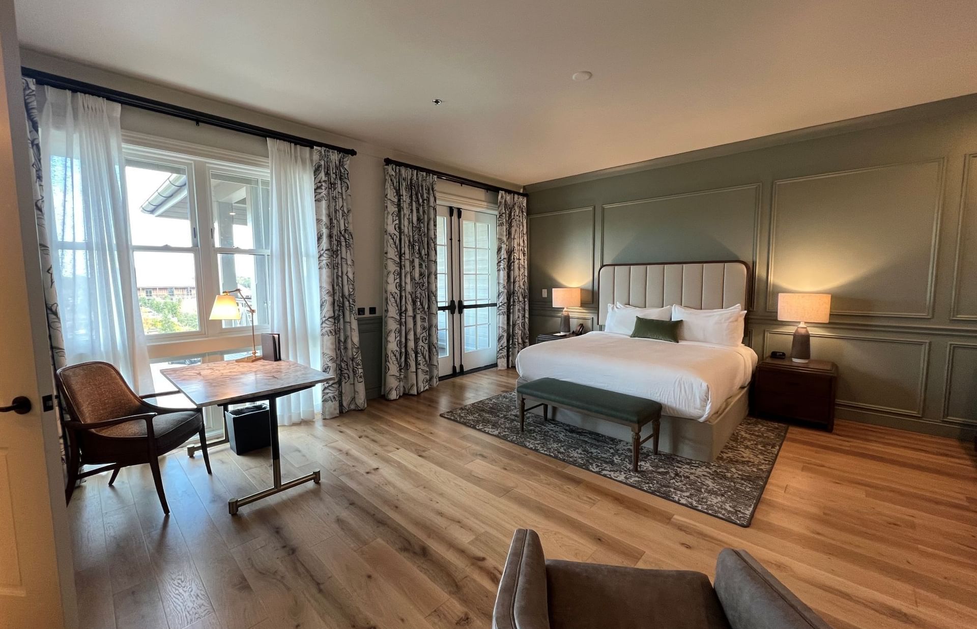 A modern bedroom with wooden floors, a large bed, a desk, and a chair by the window.