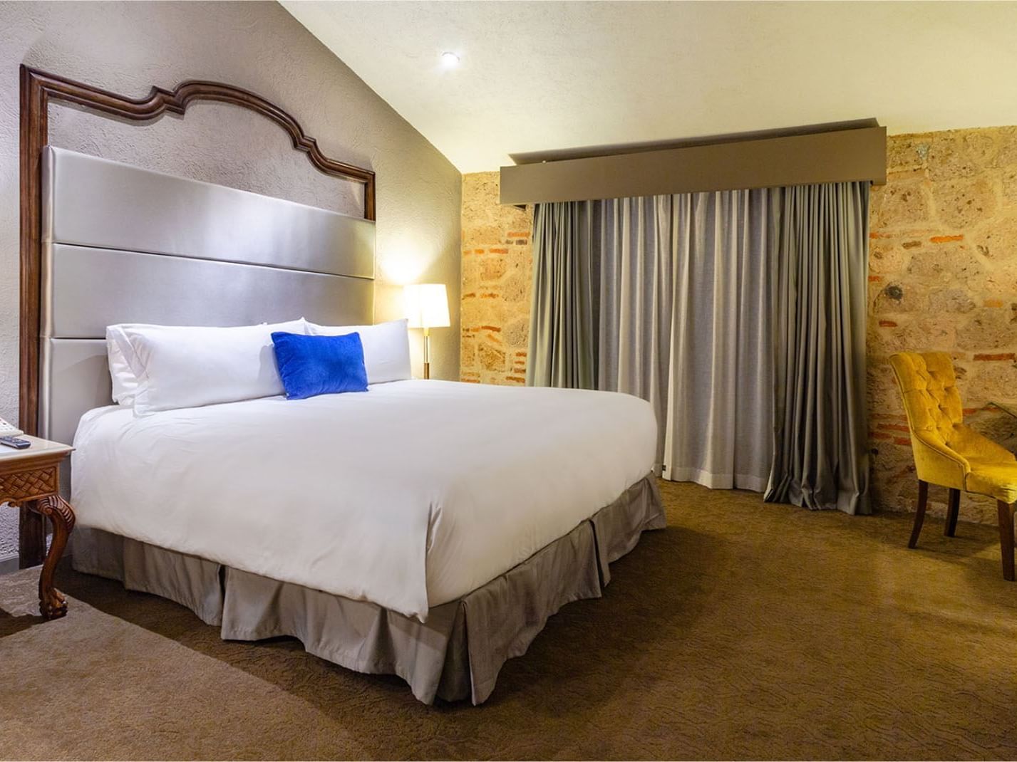 King Master Suite, bed against a rustic stone wall with elegant grey drapery at the Quinta Real Guadalajara