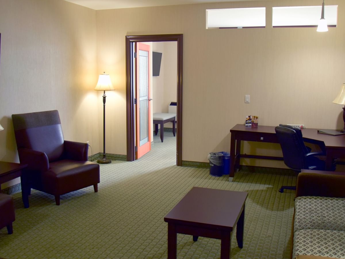 A hotel room with couch, desk, chairs, TV, and a visible bedroom area.