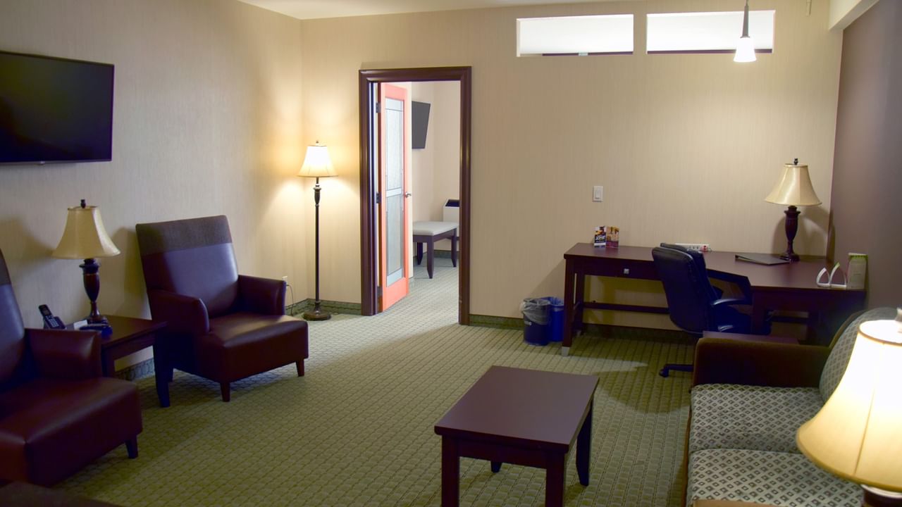 A hotel room with couch, desk, chairs, TV, and a visible bedroom area.
