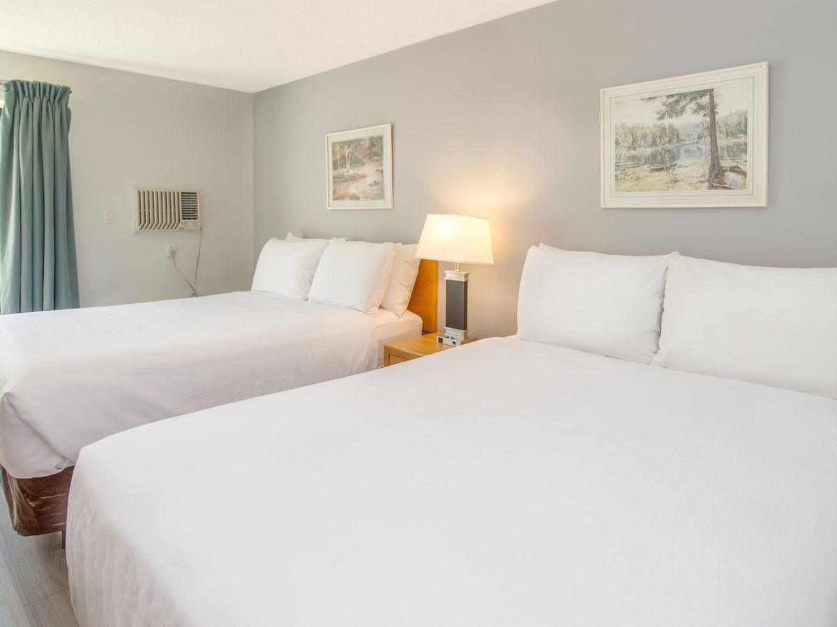 Two beds with white linens in a room with gray walls, two framed paintings, and a lamp.