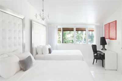 Minimalist Ocean Premium Suite Beachfront room with two white beds, large windows, sleek desk, and a lamp at Le Cameleon