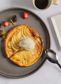 Warm apple tart topped with ice cream, fresh berries, and a side of black coffee on a gray plate at Téséo Restaurant & Bar