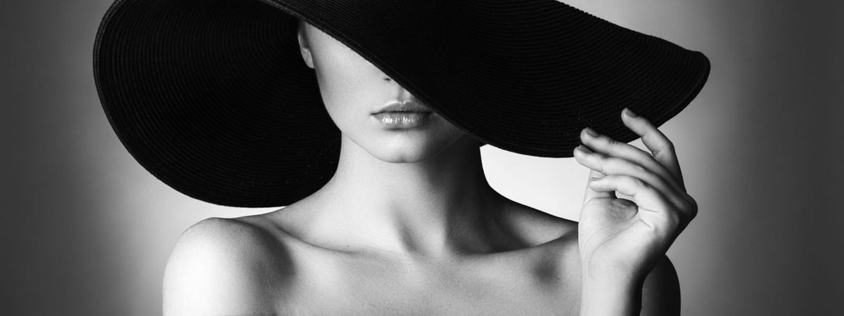 Black and white portrait of a woman wearing a wide-brimmed hat and off-shoulder dress with elegant styling.