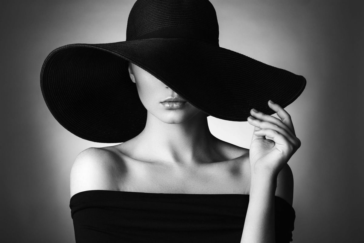 Black and white portrait of a woman wearing a wide-brimmed black hat and strapless dress 