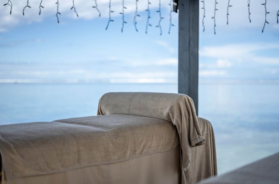 Massage table with a beige towel by a wooden post under string lights at Warwick Fiji Resort and Spa