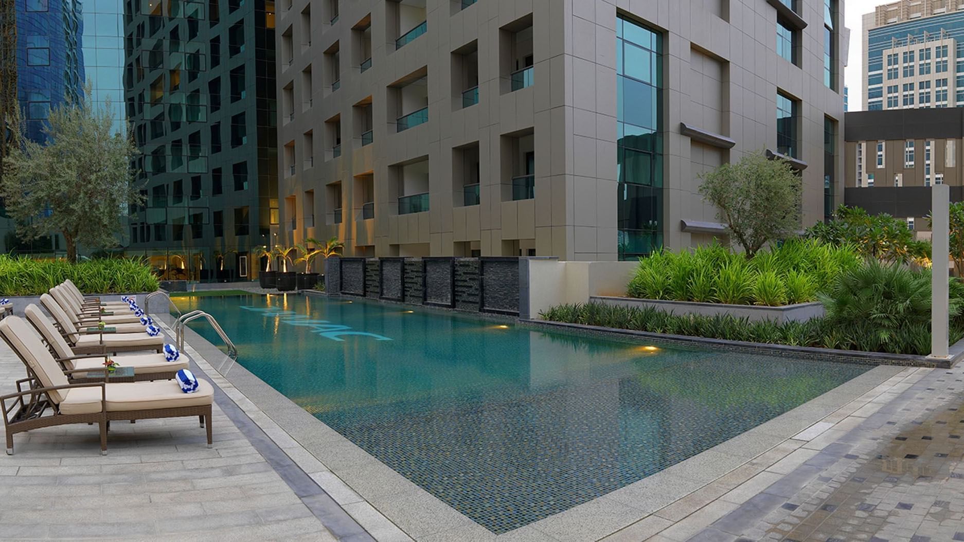 Outdoor pool area surrounded by lounge chairs at DAMAC Maison Cour Jardin