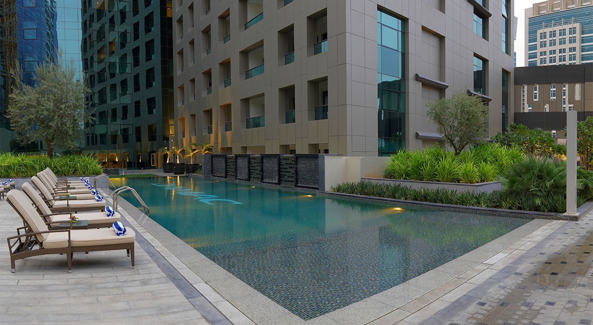 Outdoor pool area with loungers by modern high-rise buildings at DAMAC Maison Cour Jardin en Dubai