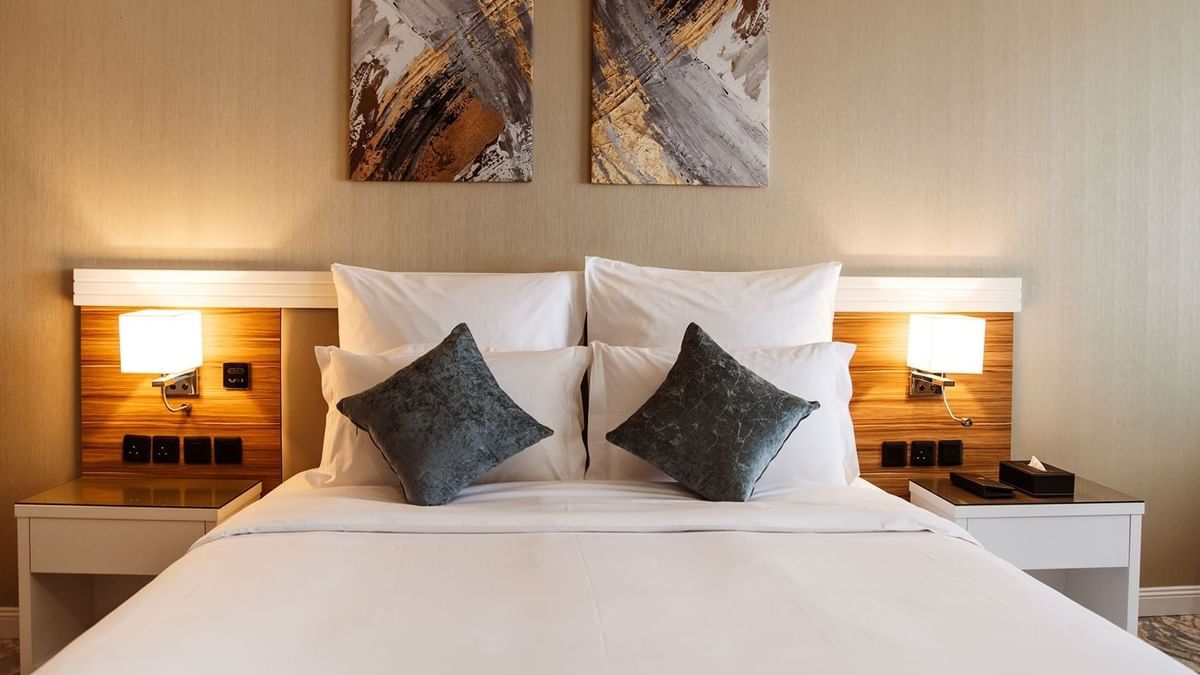Plush bed with grey cushions by wooden nightstands in Superior King / Queen Room at Cantonal Hotel by Warwick Riyadh