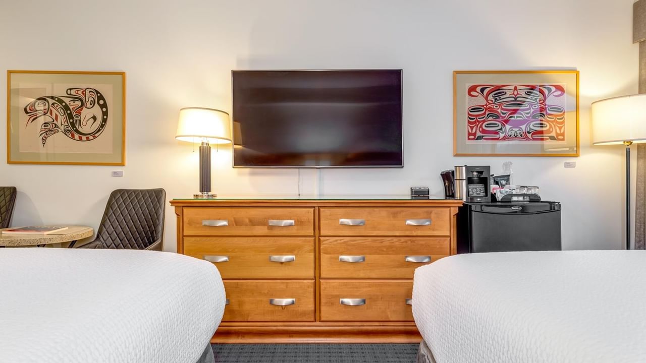 A hotel room with two beds, a dresser with a TV, and two framed artworks on the wall.