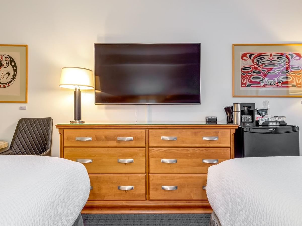 Two beds, a dresser with a TV, and framed art on the walls in a hotel room.