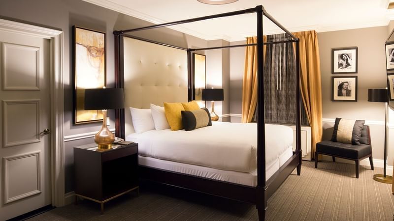 Elegant hotel bedroom with canopy bed, white linens, and modern decor.