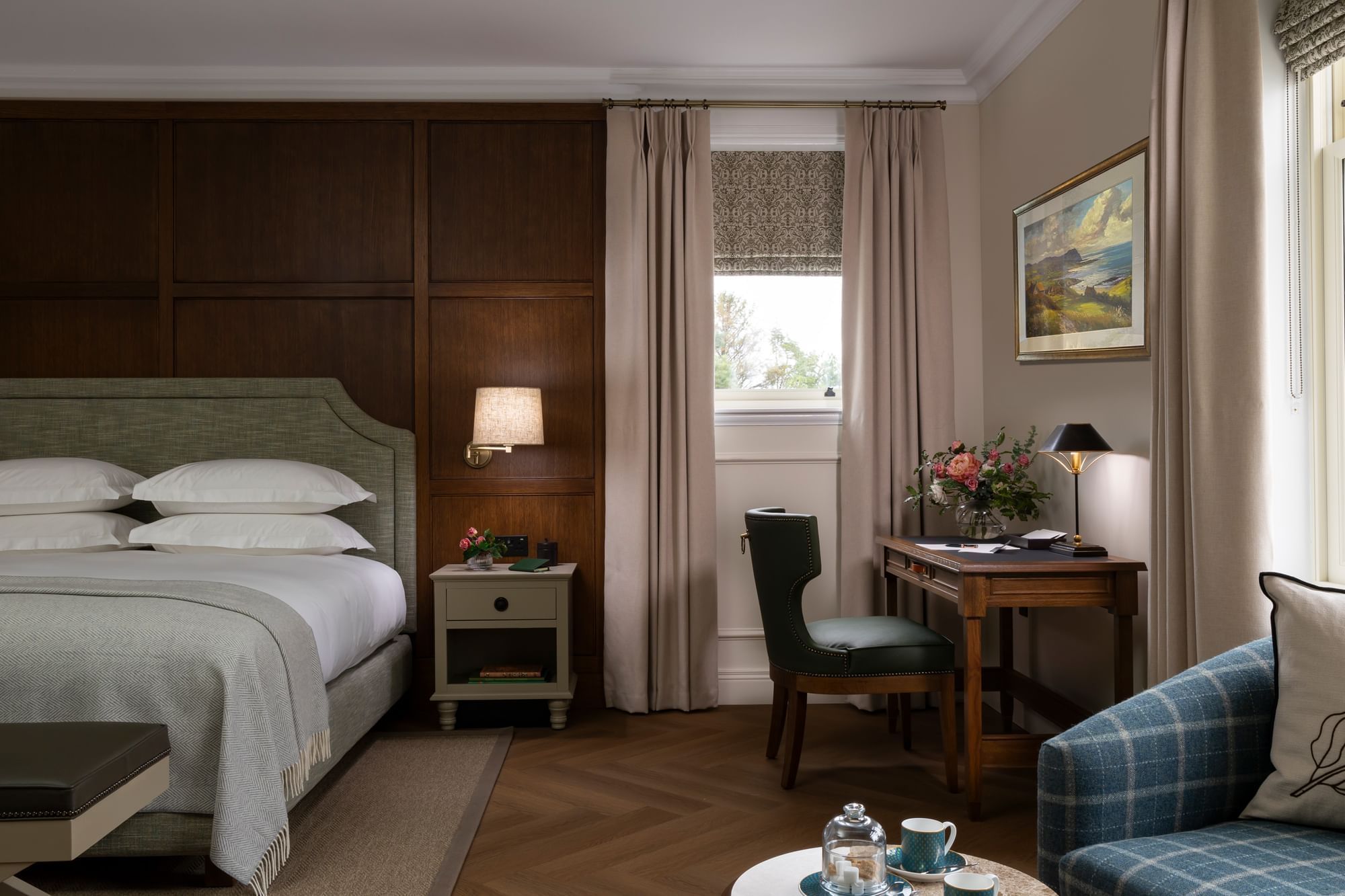 A beautiful guest room with a writing desk, checkered armchairs, and a large bed at Dunluce Lodge