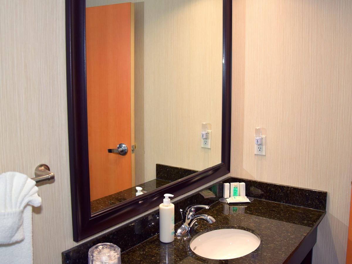 A bathroom sink with a mirror, towel, and soap bottle.