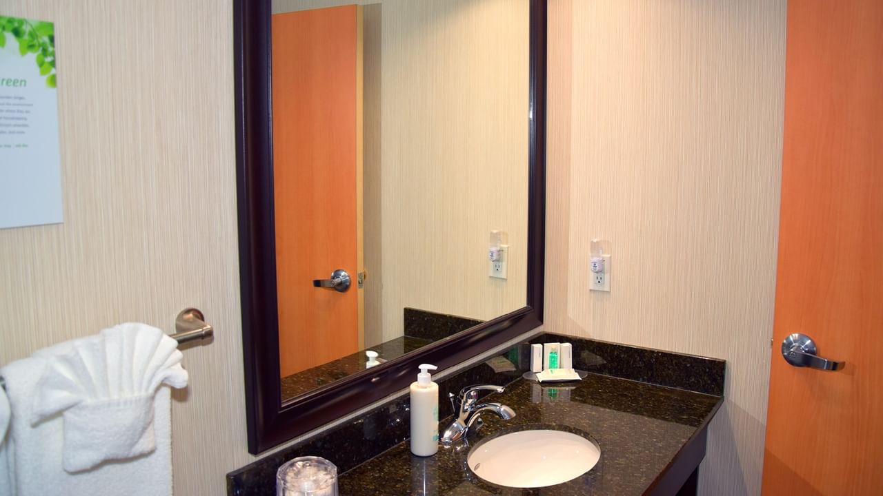 A bathroom sink with a mirror, towel, and soap bottle.