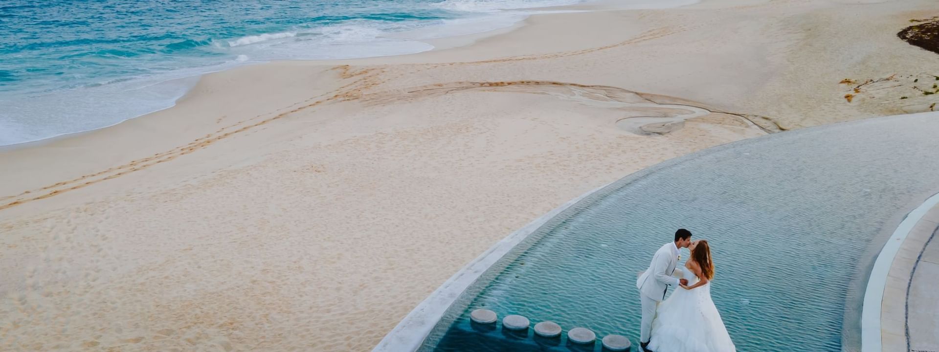 A newly married couple embracing by an infinity pool overlooking a serene beach at Mountain View Grand Resort & Spa